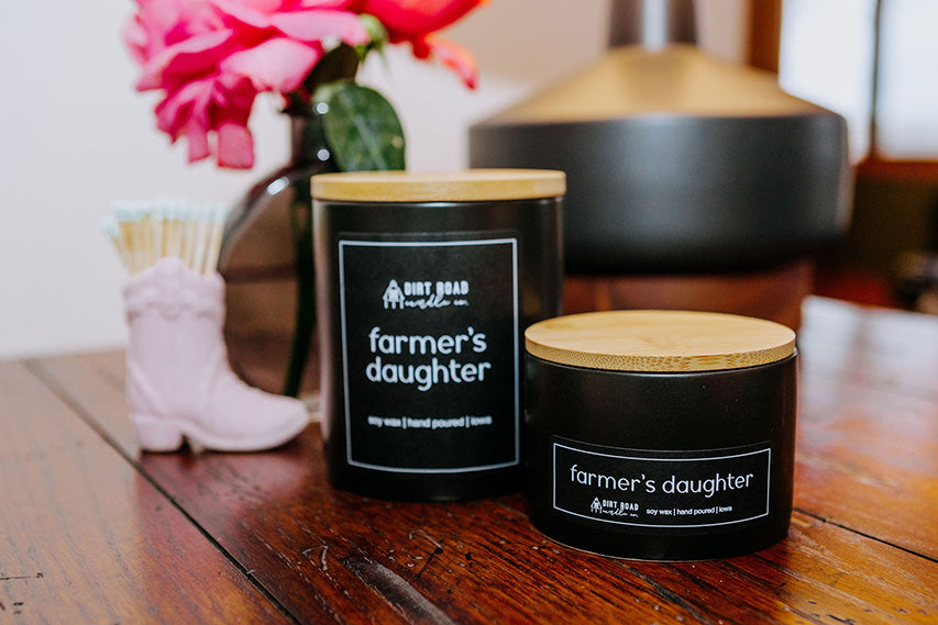 Farmer's Daughter candle in a matte black container with a bamboo lid placed on a rustic wooden table