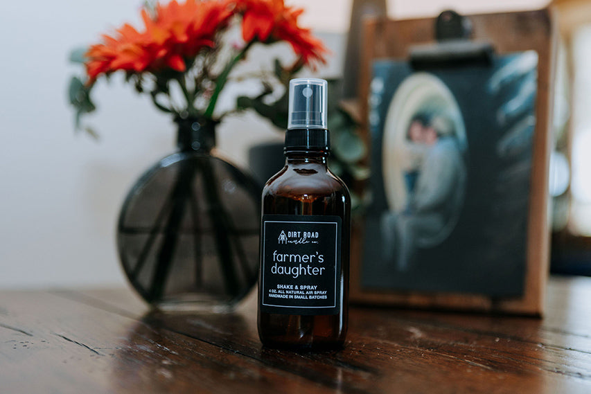 Farmer's Daughter natural room air spray in an amber glass bottle sitting on a rustic wooden table.