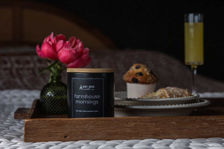 Farmhouse Mornings soy wax candle in a black jar with a wooden lid, sitting on a wooden breakfast tray.