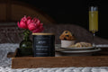 Farmhouse Mornings soy wax candle in a black jar with a wooden lid, sitting on a wooden breakfast tray.