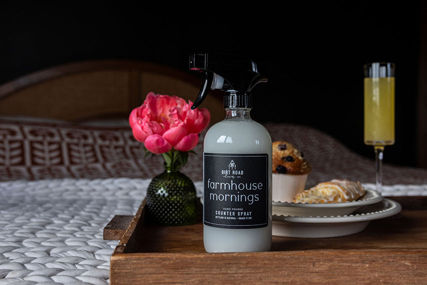 Farmhouse Mornings counter spray bottle with black trigger on a wooden tray with a floral arrangement and breakfast items.