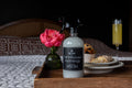 Farmhouse Mornings counter spray bottle with black trigger on a wooden tray with a floral arrangement and breakfast items.