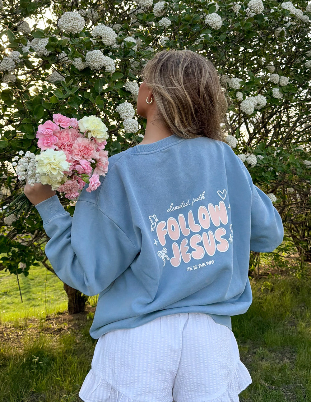 A person wearing a Follow Jesus unisex knit crewneck in pale-pink, styled for a casual preppy look.
