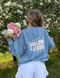 A person wearing a Follow Jesus unisex knit crewneck in pale-pink, styled for a casual preppy look.