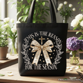 Jesus Is the Reason Christmas tote bag featuring a gold coquette bow and cross design on canvas.