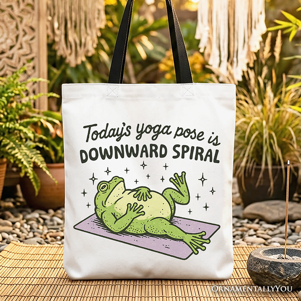 A white cotton tote bag featuring a green frog in a yoga pose labeled Downward Spiral.