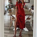 A woman wearing a black and red striped loose V-neck midi dress with a high side slit.