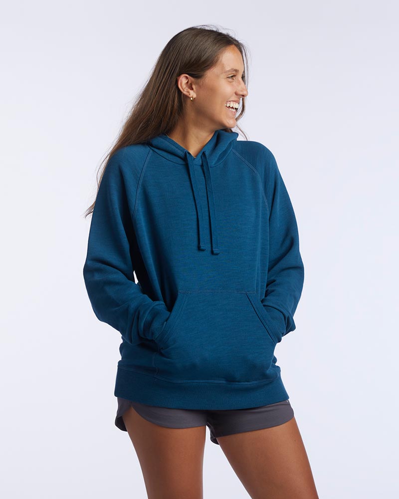 A woman wearing a relaxed fit teal pullover hoodie with a front kangaroo pocket and graphic detailing on the side.