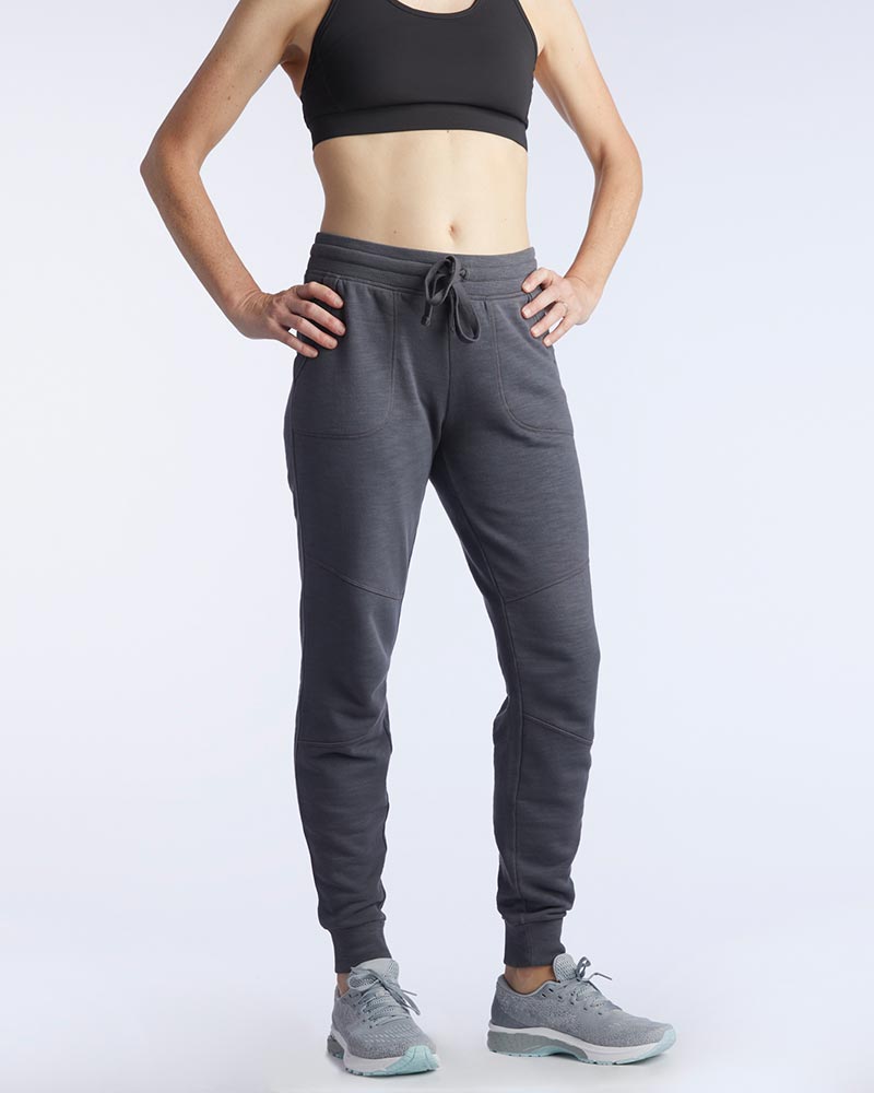 Side view of a woman wearing charcoal grey athletic joggers with Goal Five branding on the lower leg.