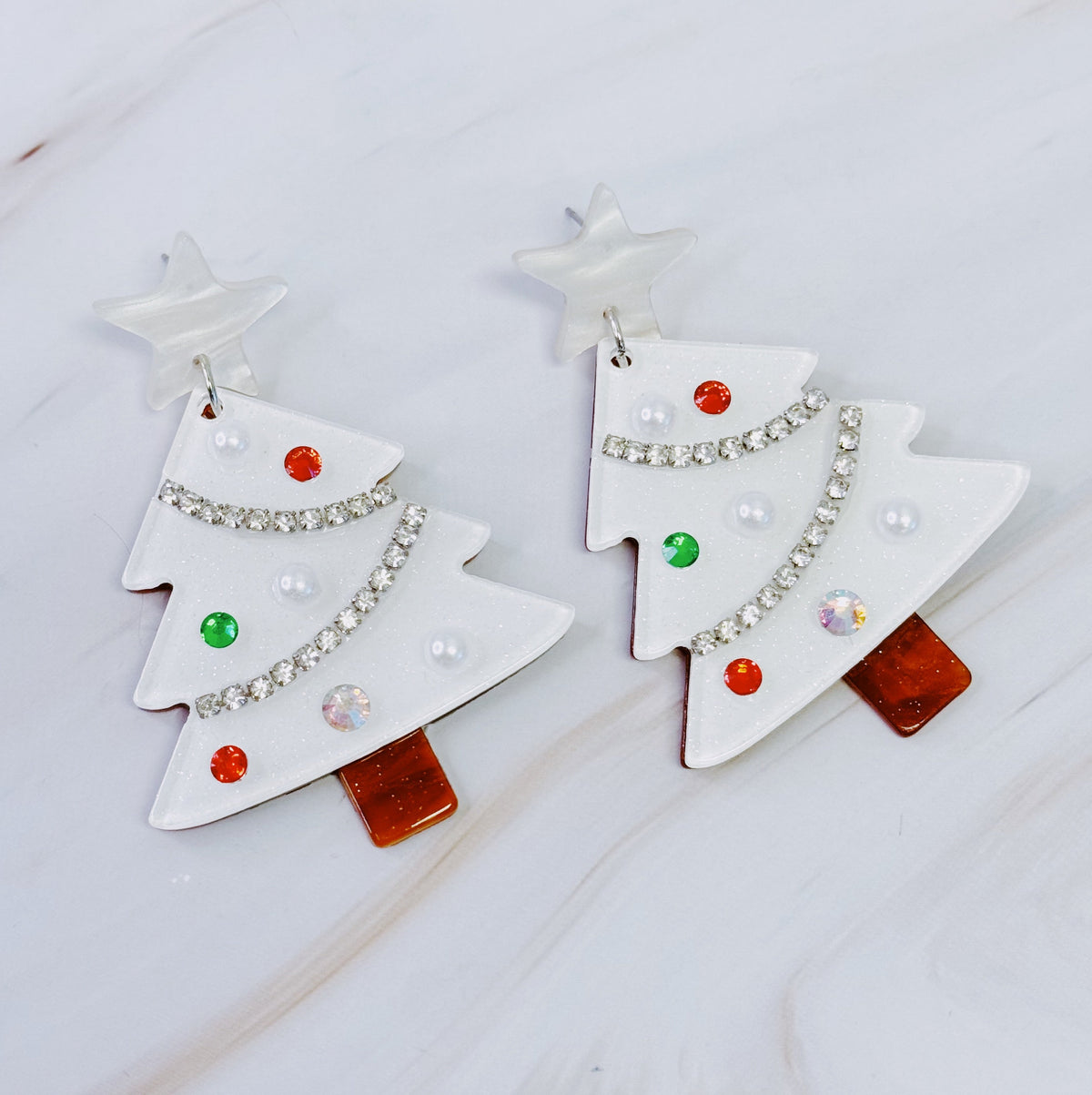 A pair of white acrylic Christmas tree shaped dangle earrings with star tops and colorful crystal ornaments.