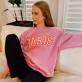 A woman wearing a pink oversized crewneck sweatshirt with PARIS printed on the chest