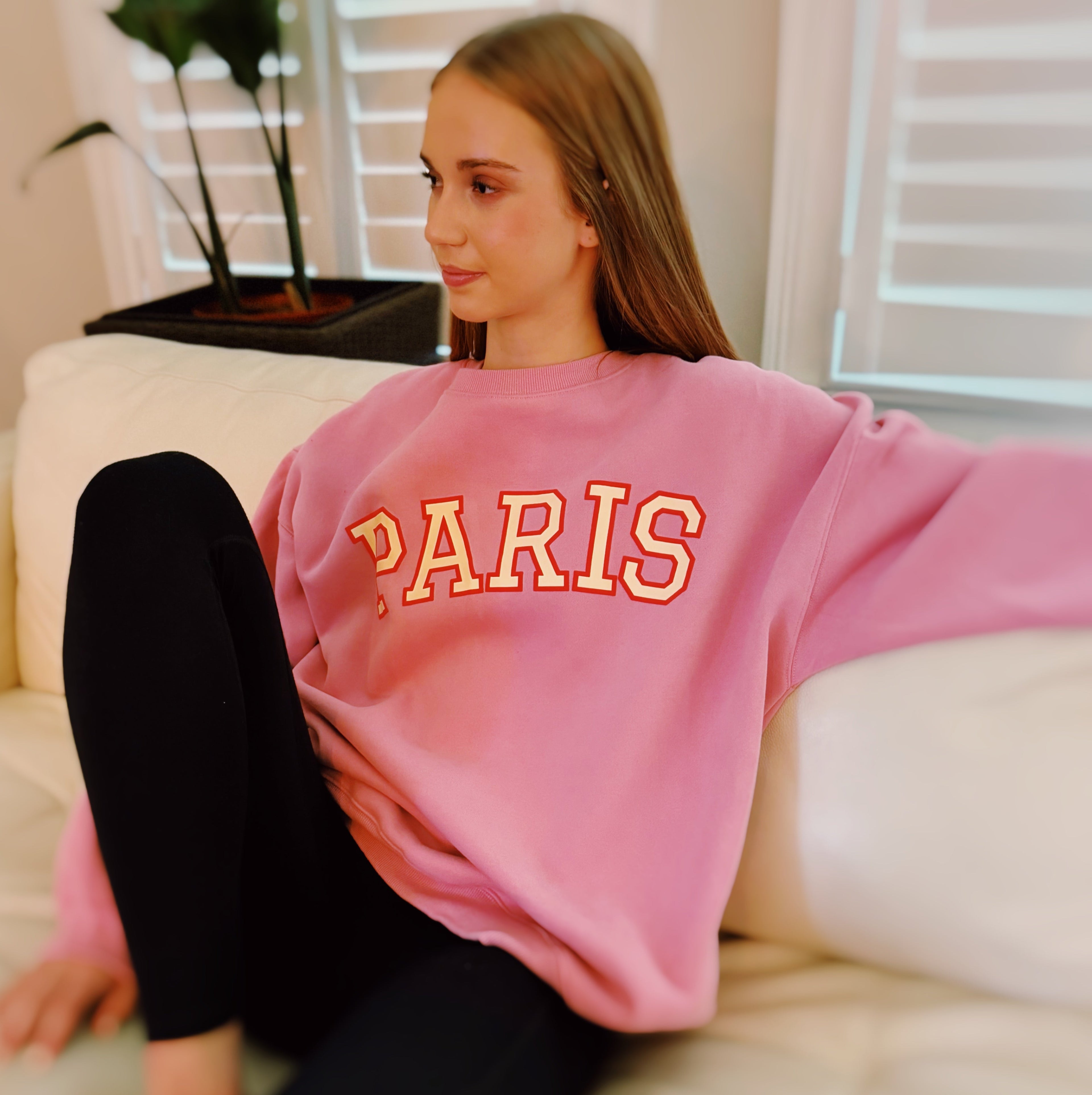A woman wearing a pink oversized crewneck sweatshirt with PARIS printed on the chest