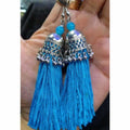 Fashionable blue hanging thread jhumka earrings on a plain background.