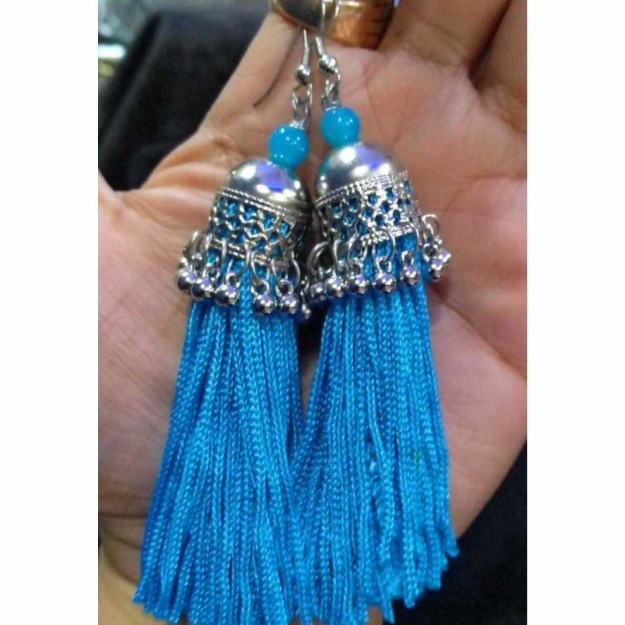 Fashionable blue hanging thread jhumka earrings on a plain background.
