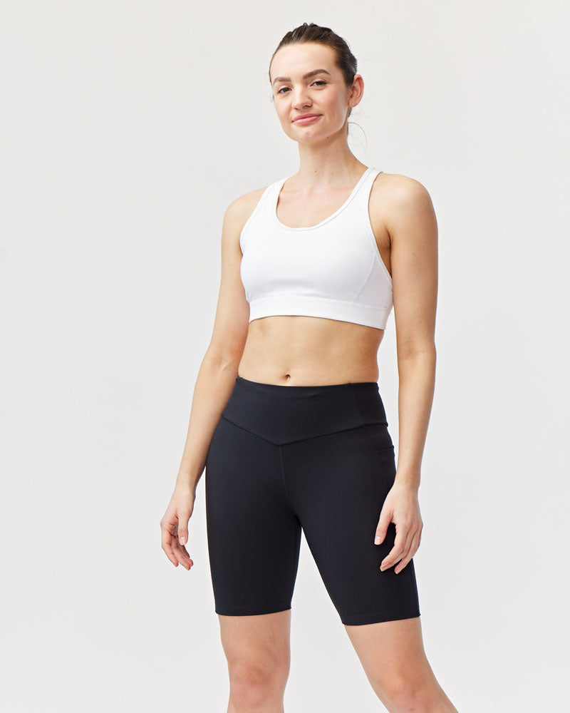 Back view of a woman wearing black 8-inch compression bike shorts with side pockets and a small logo detail.