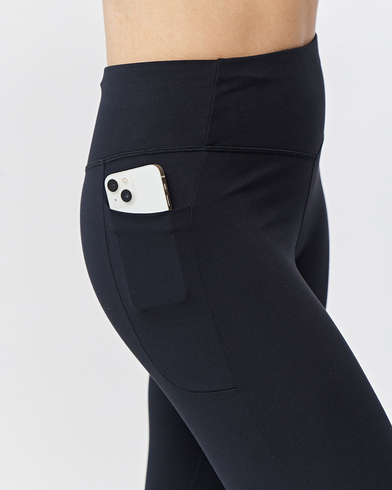 Side view of woman wearing black high-rise cropped athletic leggings with a phone stored in the side pocket.