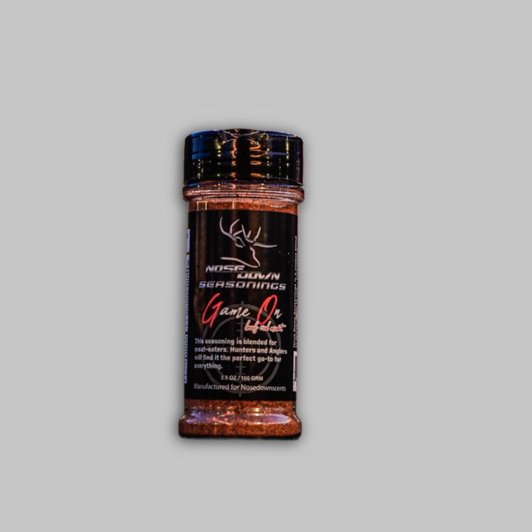 A 3.5oz jar of Game On Seasoning with a black label, red and white typography, resting on a rustic wooden surface.