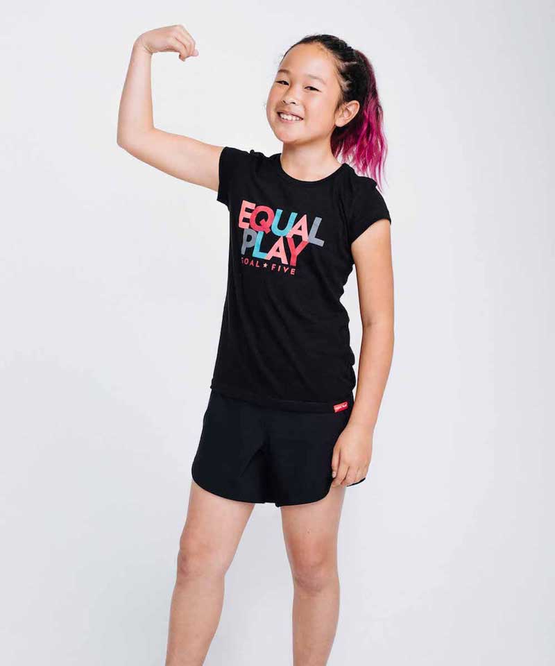 A young girl with pink-streaked hair wearing a black short-sleeved t-shirt with Equal Play graphic text.