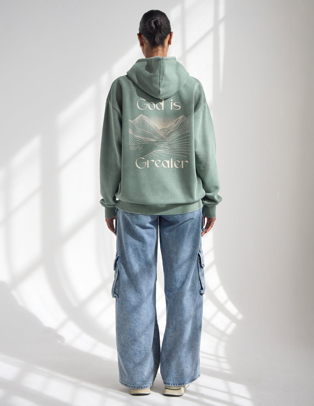 Front view of Elevated Faith God Is Greater unisex hoodie in moss green with heavy running stitch embroidery.