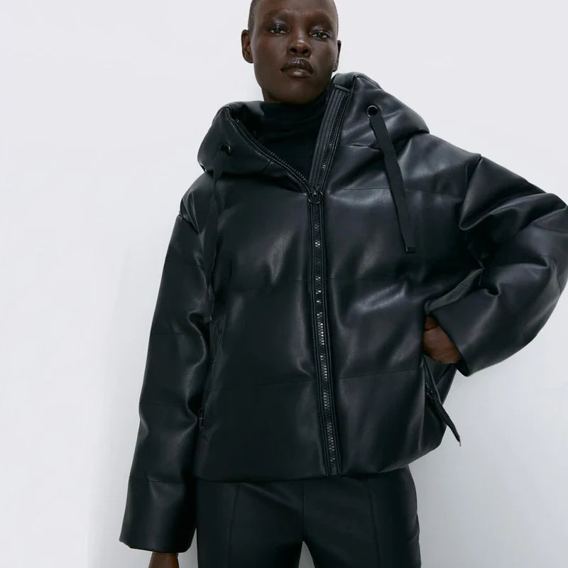 Woman wearing a black faux leather hooded puffer parka jacket with a front zipper closure, posed against a white background.
