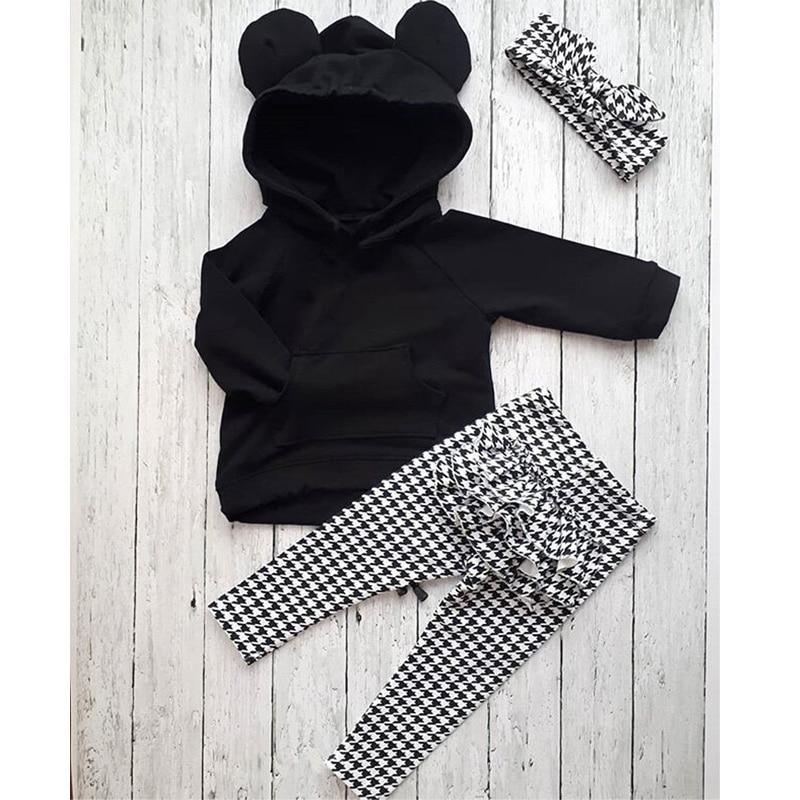 Toddler girl wearing a black hooded pullover with ruffles plaid pants and a matching headband