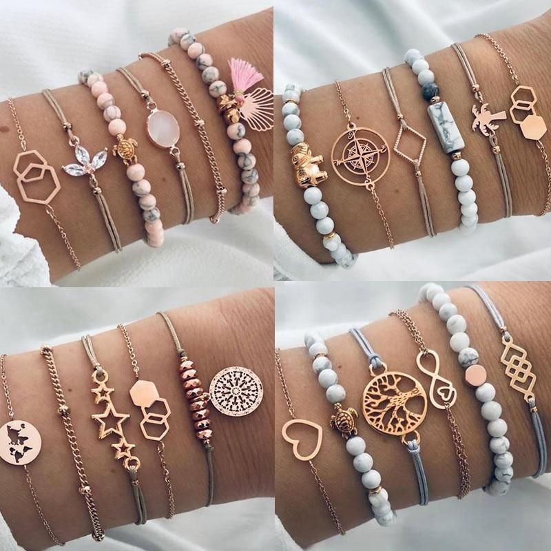 A layered set of gold-plated bohemian bracelets featuring tree of life and infinity charms with neutral tassel accents on a model's wrist.
