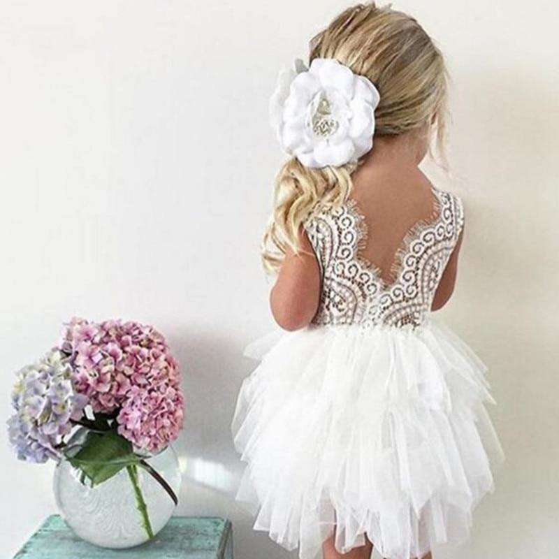 Toddler girl wearing a white lace and tulle birthday dress with a matching floral headband for a cake smash photo session.