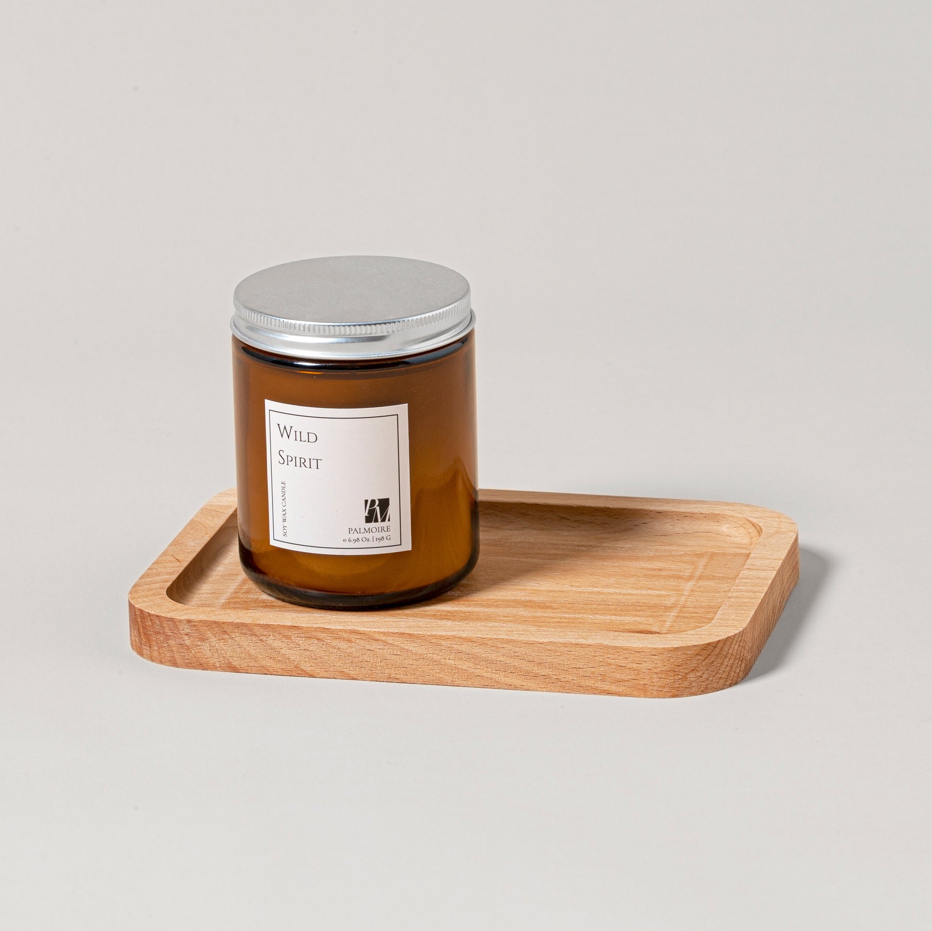Wild Spirit scented soy wax candle in an amber glass jar resting on a natural wooden tray.