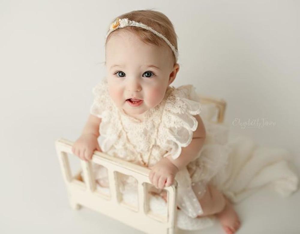 Baby girl wearing a cream lace ruffle romper with tutu detail, long-sleeved bodice, and button-bottom closure.