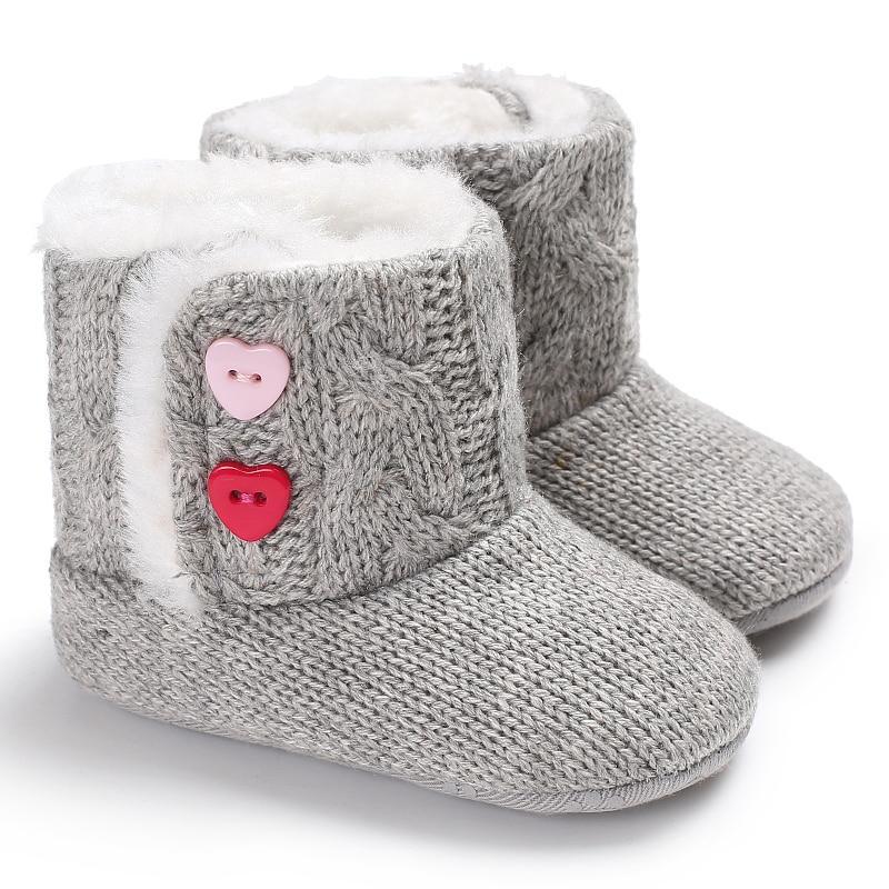 Baby girl wearing soft grey knitted anti-slip boots on a neutral background