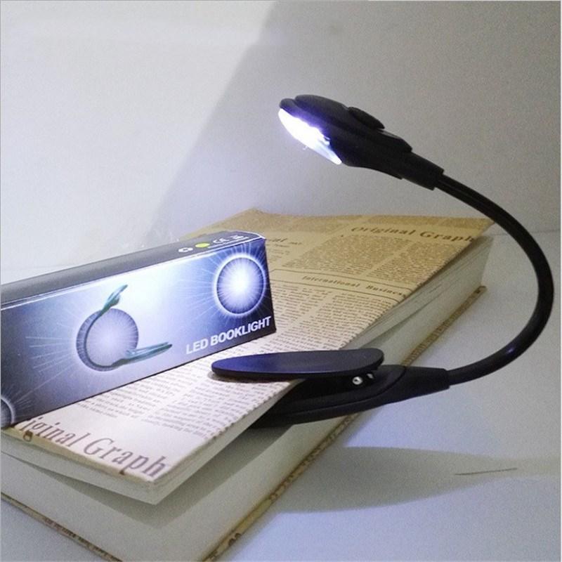 Minimalist black portable LED clip-on reading light attached to a book cover in a bedroom setting.