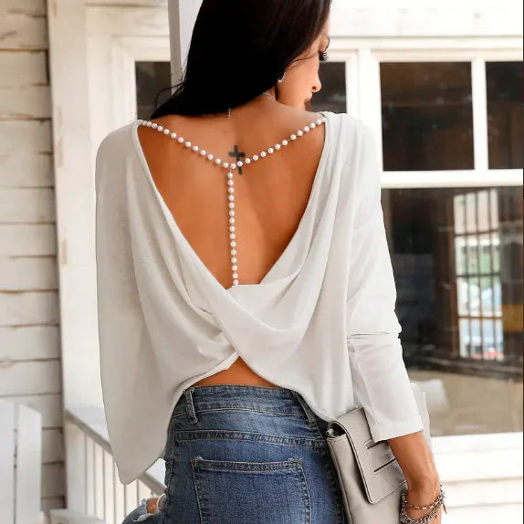 A woman wearing a backless long sleeve t-shirt with pearl strap details on her back, styled with blue jeans.