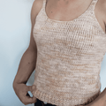 A woman wearing a handmade bohemian knit tank top in soft peach and cream variegated tones.