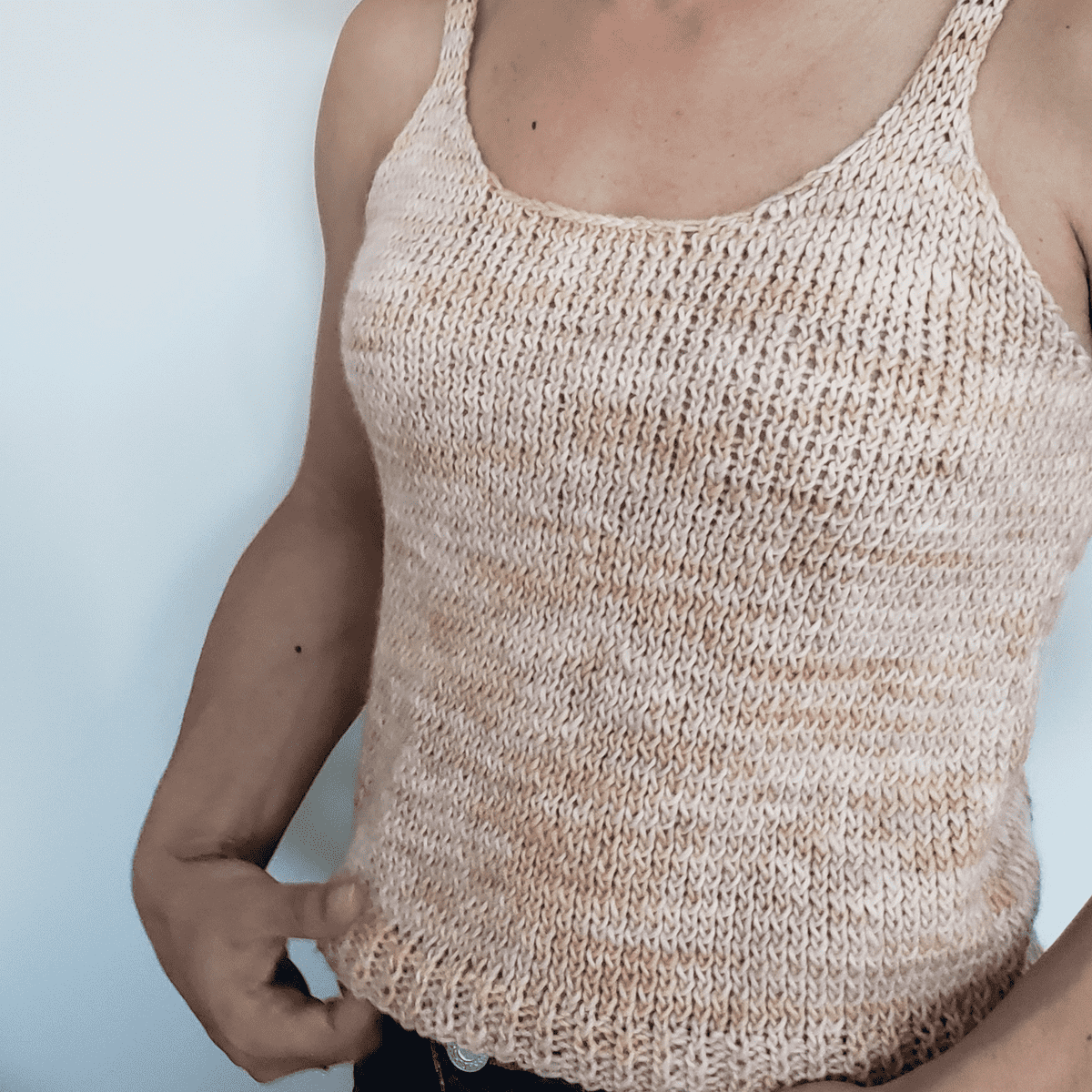 A woman wearing a handmade bohemian knit tank top in soft peach and cream variegated tones.