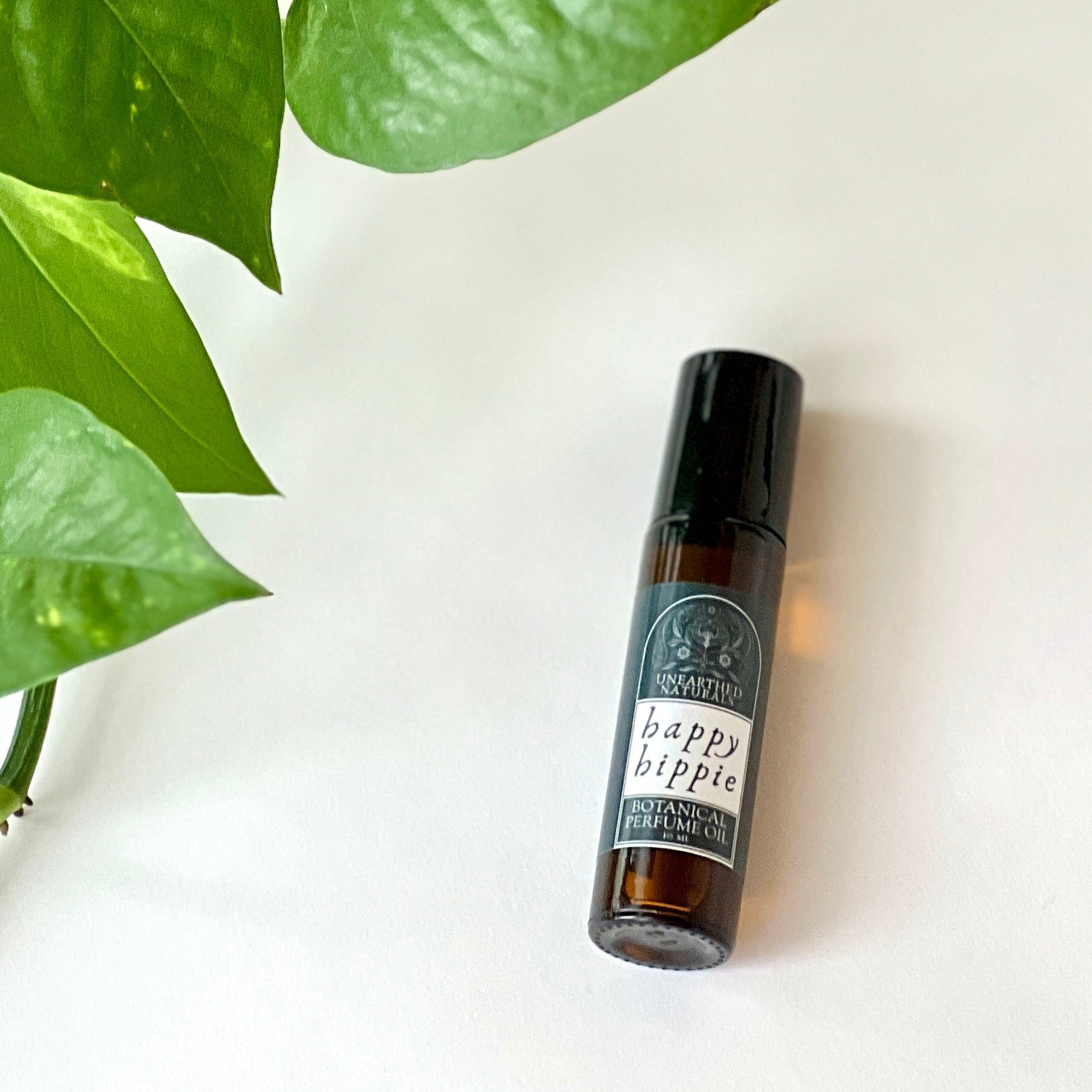 Happy Hippie Botanical Perfume Oil 10ml amber glass bottle next to a green plant