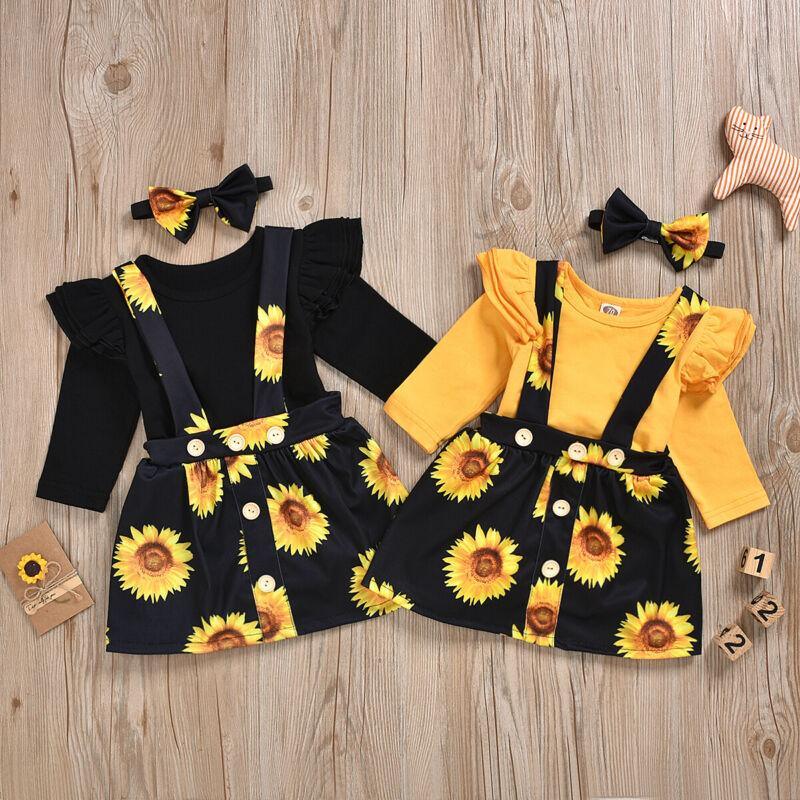 Baby girl wearing a yellow sunflower short-sleeve dress and floral skirt with a matching headband.