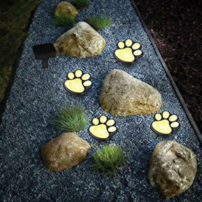 Set of 4 black paw-shaped solar LED garden lights glowing on a grass pathway