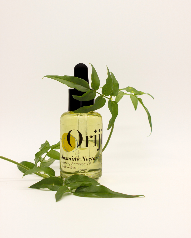 Bottle of Orijin Jasmine Nectar Calming Botanical Oil with a dropper on a white background with green foliage