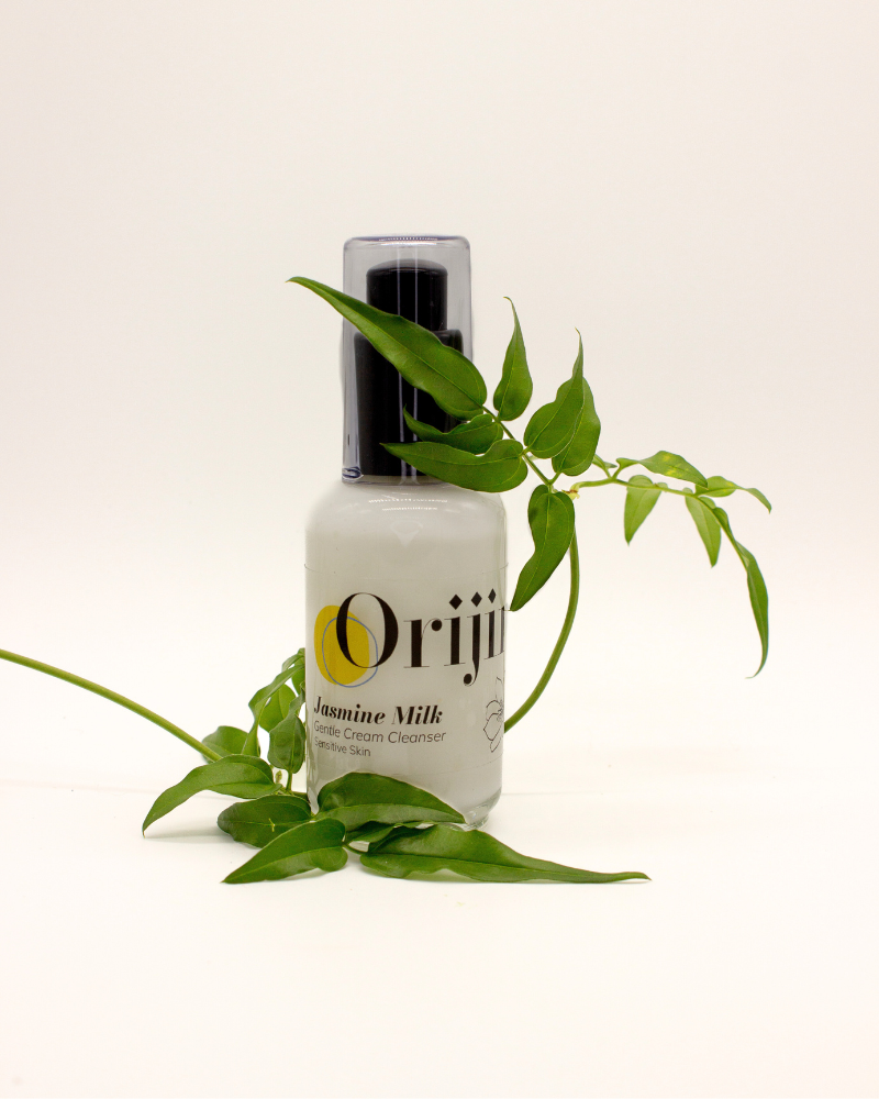 Bottle of Orijin Jasmine Milk Gentle Cream Cleanser next to green foliage.