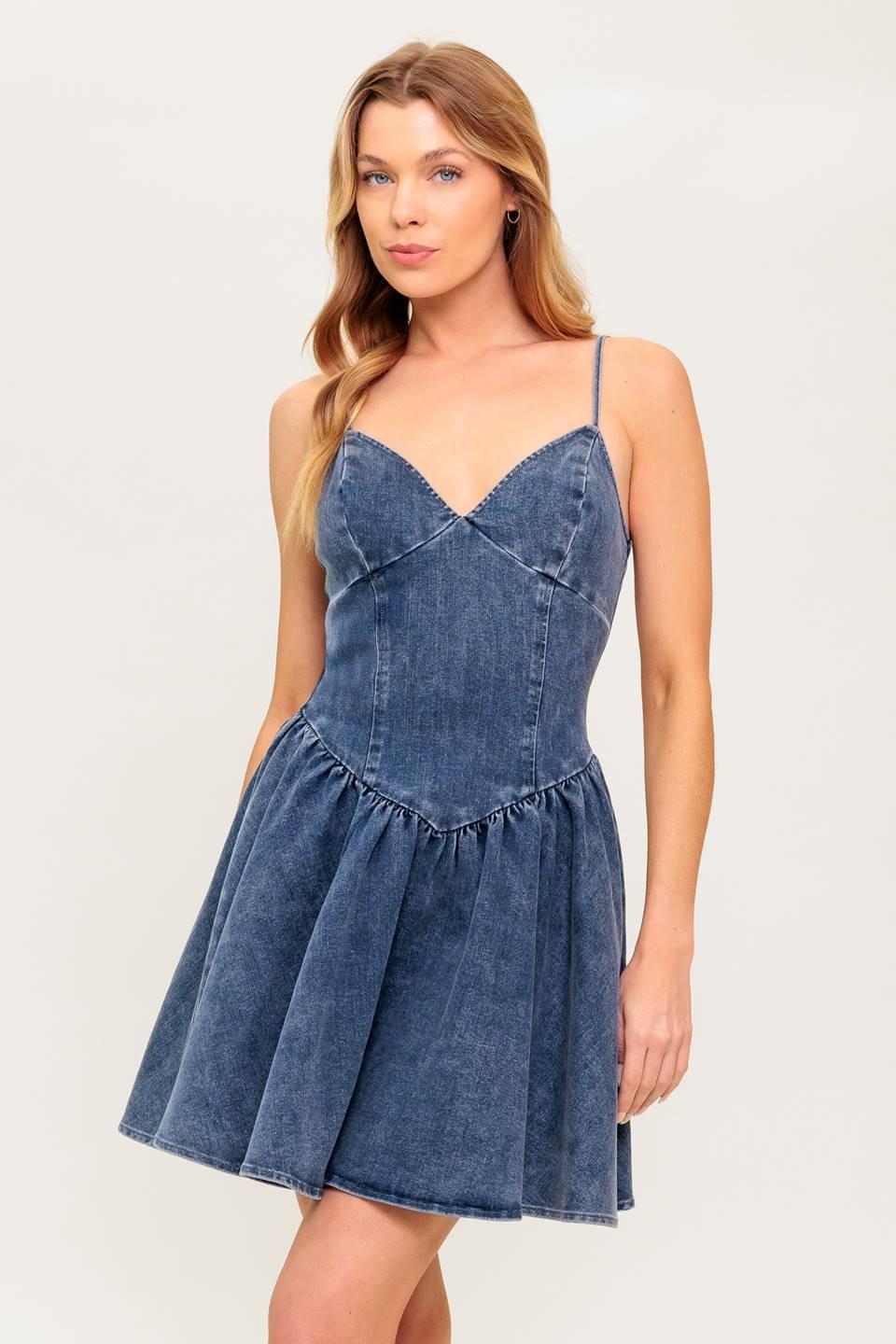 Model wearing a blue washed denim mini dress with cami straps and a basque waist, isolated on a white background.