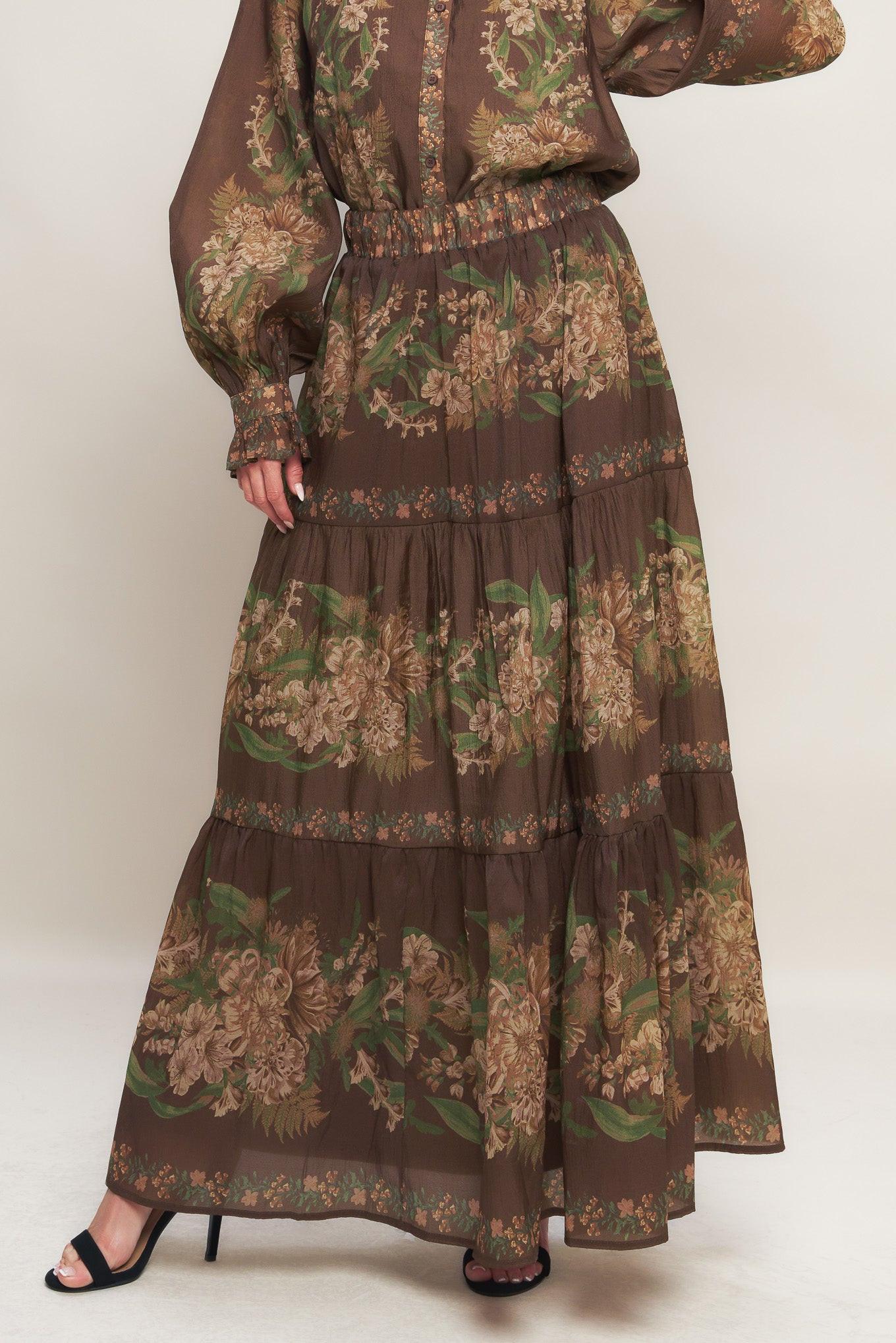 A woman wearing a brown floral print tiered woven maxi skirt with an elastic waistband.