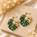 Hand-painted cream variegated monstera leaf earrings on a minimalist display