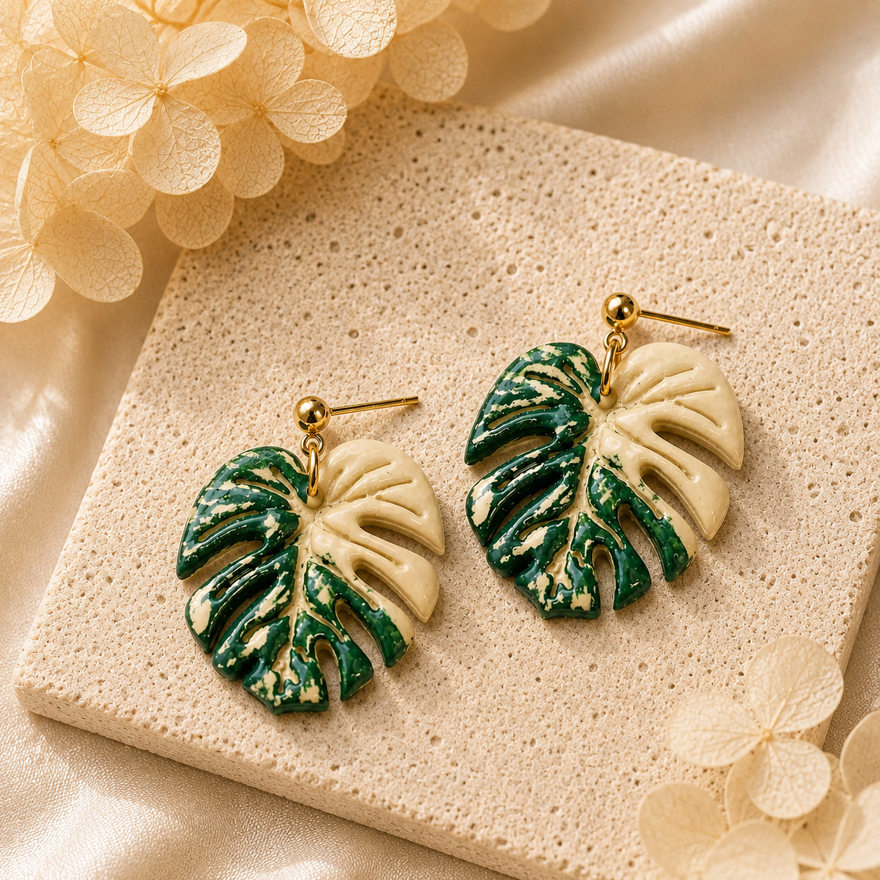 Hand-painted cream variegated monstera leaf earrings on a minimalist display