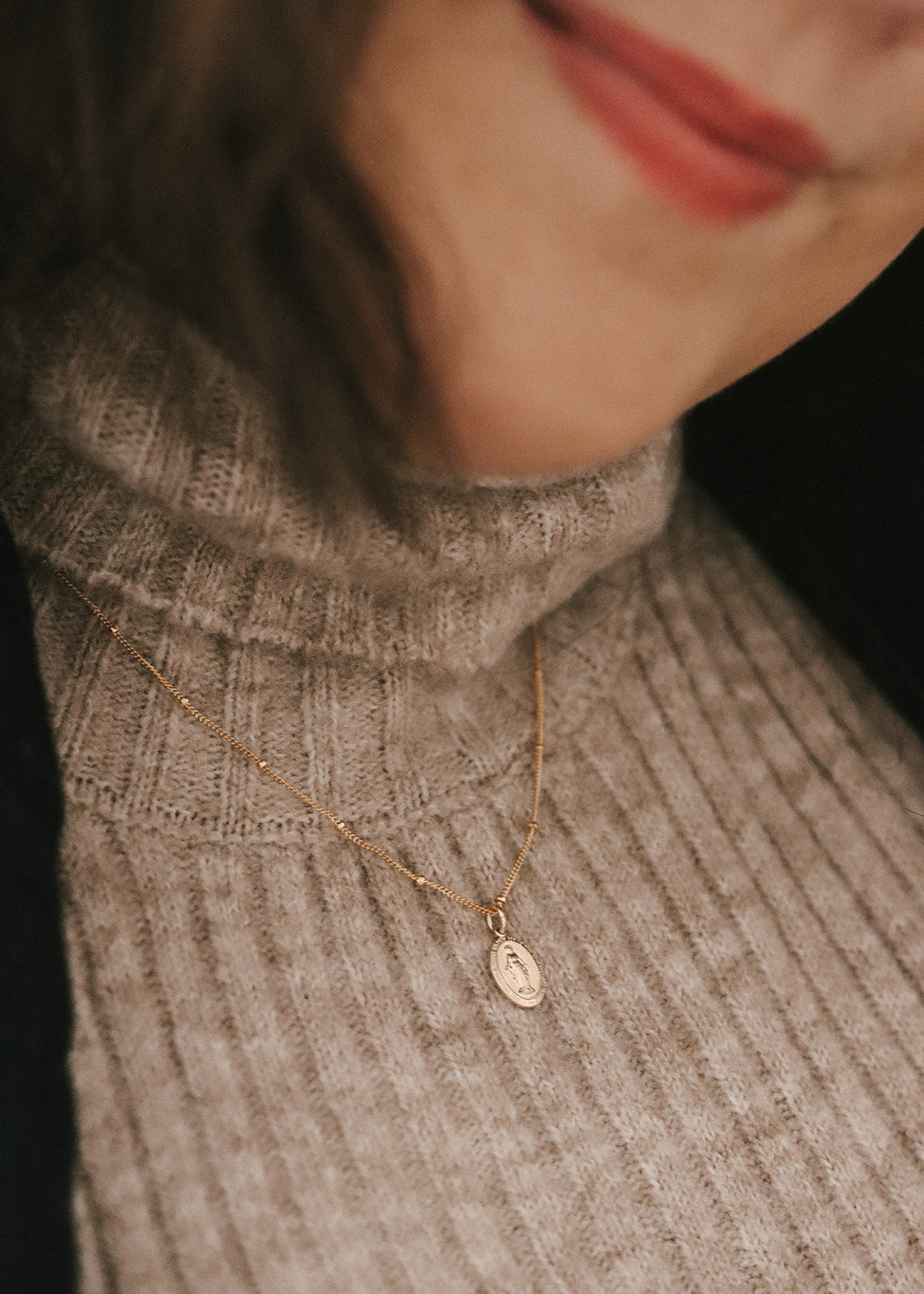 Close-up of a person wearing a gold necklace with a pendant, blurred background