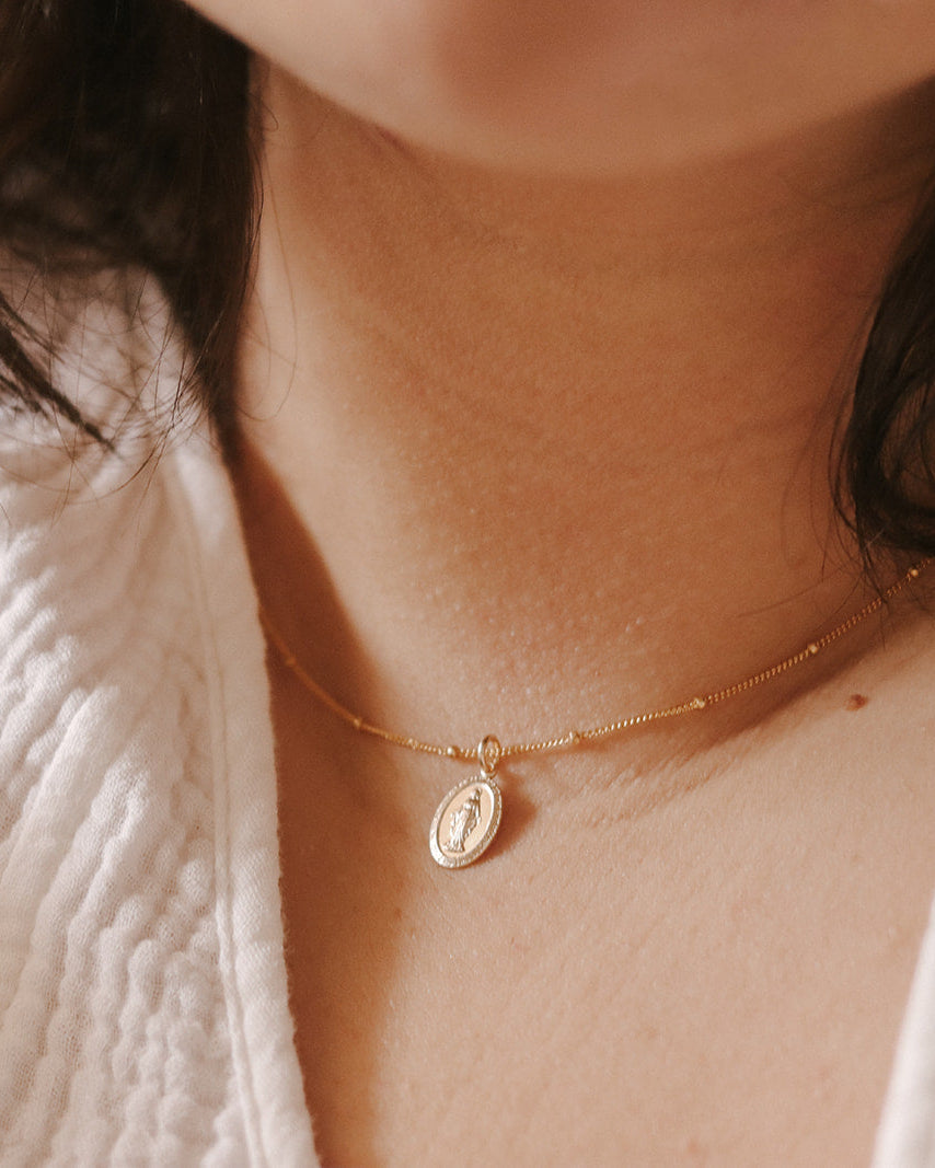 Close-up of a person wearing a delicate gold necklace with a small pendant.