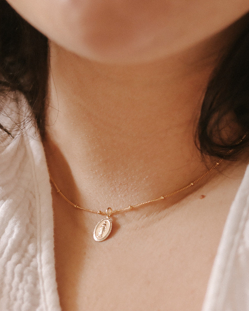 Close-up of a person wearing a gold necklace with a pendant.