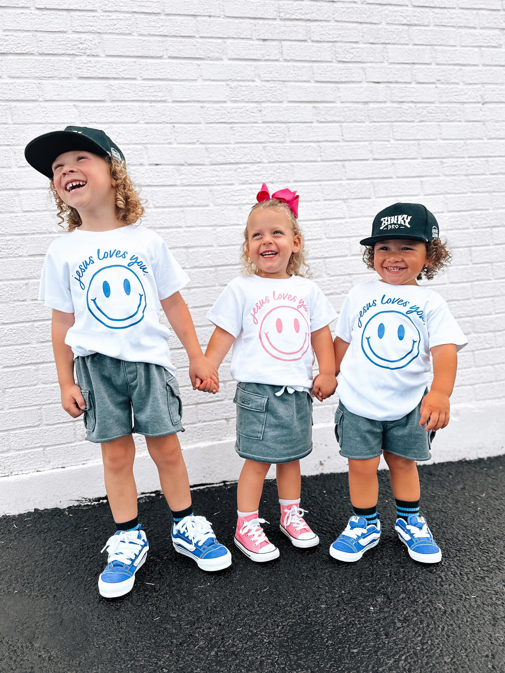 Jesus Loves You smiley face graphic toddler tee available in white, blue, and pink.