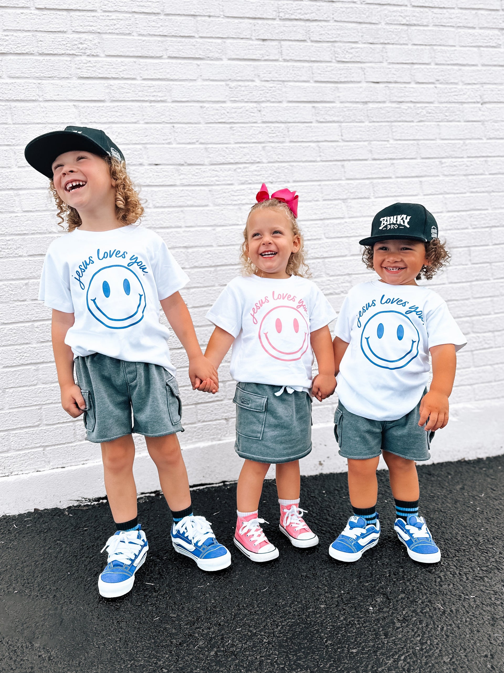 Jesus Loves You smiley face graphic toddler tee available in white, blue, and pink.
