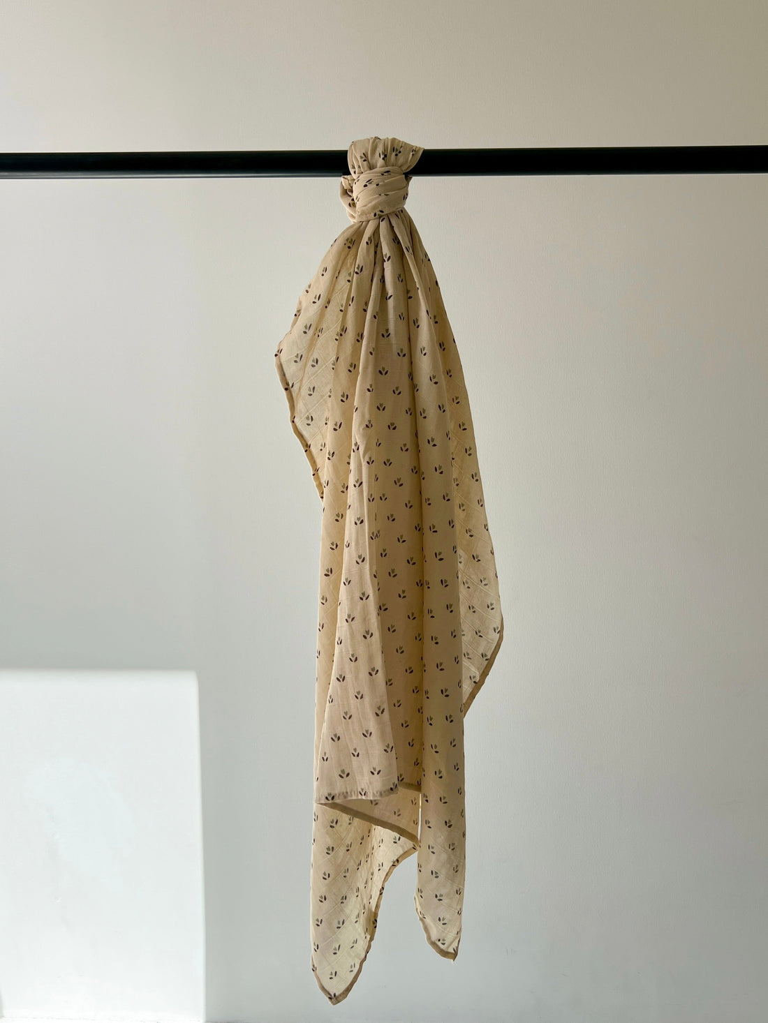 Peach Flora print muslin cotton swaddle blanket hanging over a bar