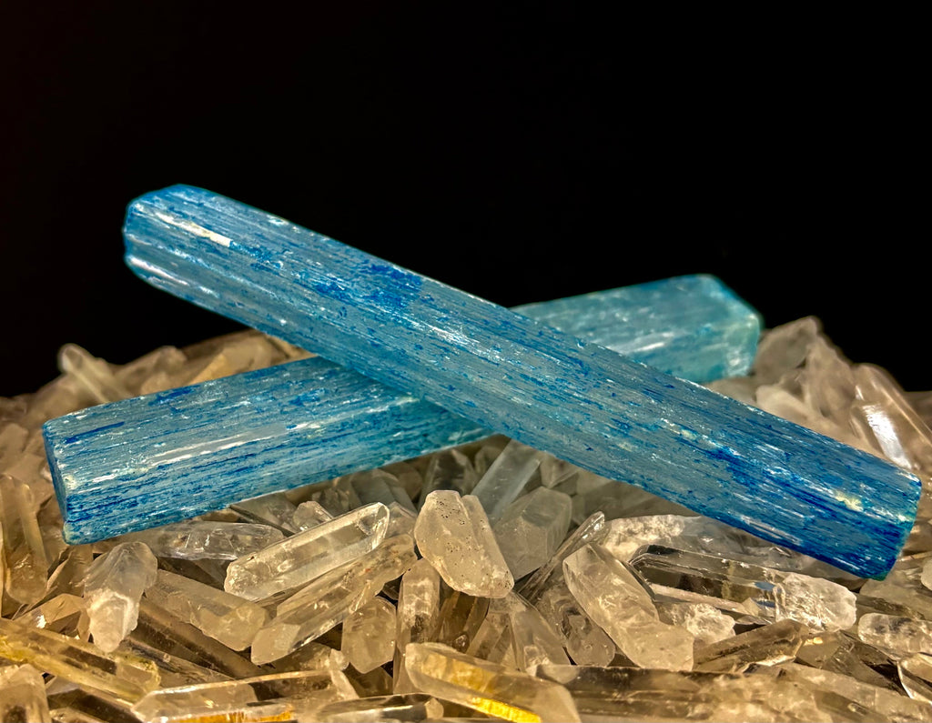 Two 6-inch blue dyed selenite charging sticks resting on a bed of smaller clear quartz crystals.